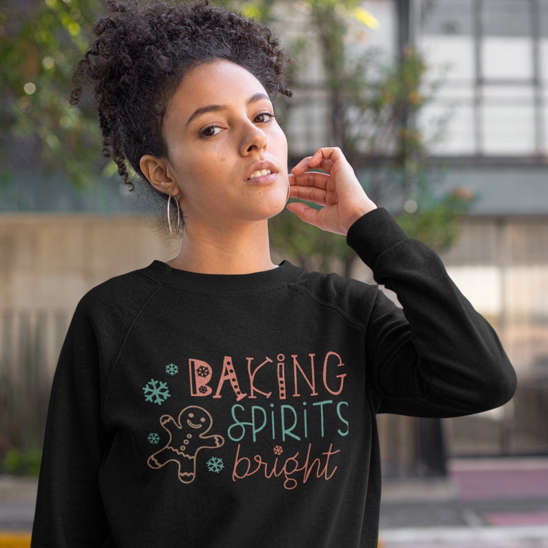 May include: Black sweatshirt with a festive design featuring a gingerbread man, snowflakes, and the text "Baking Spirits Bright".