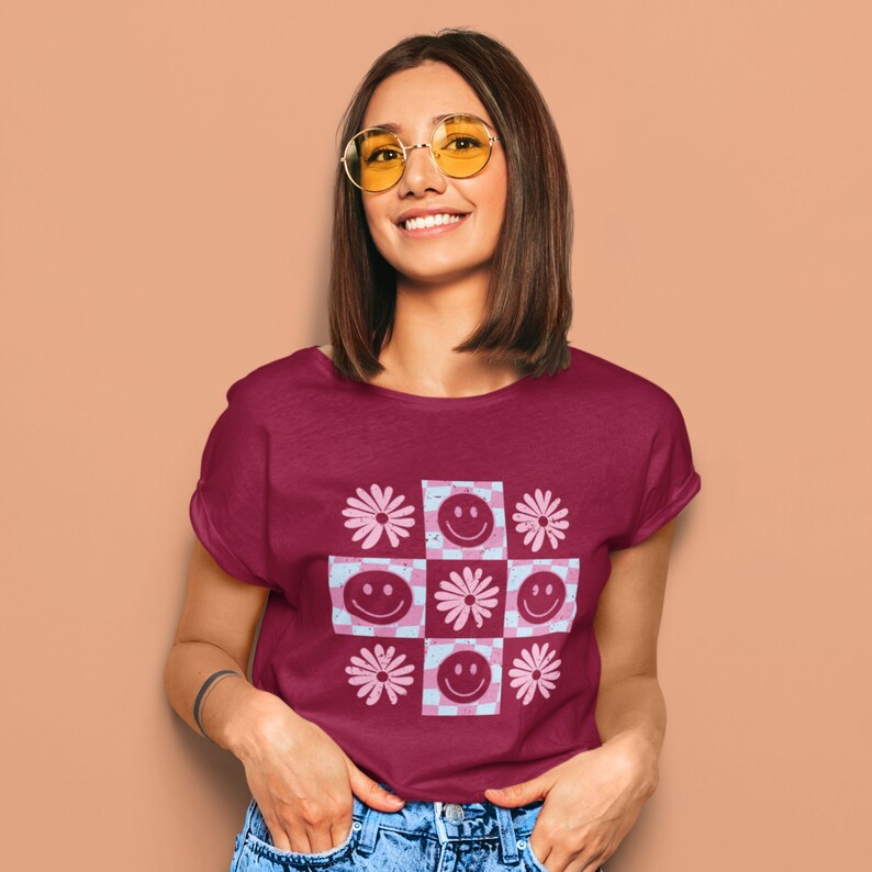 Pode incluir: Uma camiseta vinho com um padr&atilde;o xadrez rosa e azul com rostos sorridentes e flores.