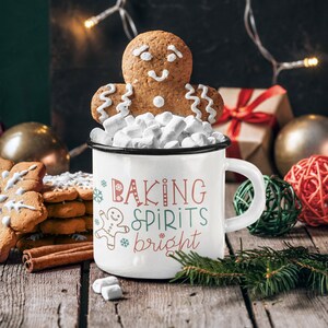 May include: White enamel mug with a black rim and handle. The mug has a gingerbread man design and the text "Baking Spirits Bright". The mug is filled with marshmallows and a gingerbread man cookie is on top.