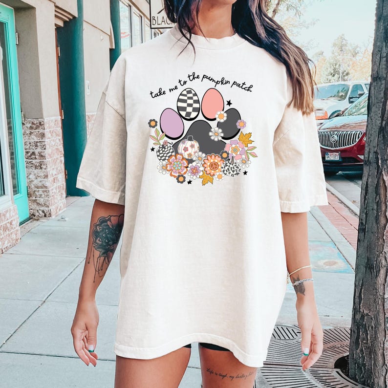 May include: A white oversized t-shirt with a paw print design featuring pumpkins, flowers, and the text "take me to the pumpkin patch".