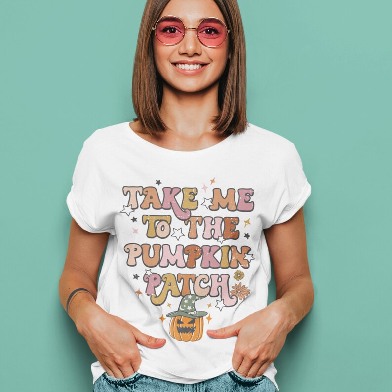 May include: White t-shirt with a graphic print that says "Take Me To The Pumpkin Patch" in a retro font with stars and flowers. A cartoon pumpkin with a witch's hat is below the text.