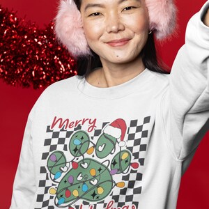 Puede incluir: Sudadera blanca con un dise&ntilde;o de huella de pata verde y el texto "Feliz Navidad". La huella de pata est&aacute; decorada con luces de Navidad de colores y un gorro de Pap&aacute; Noel.