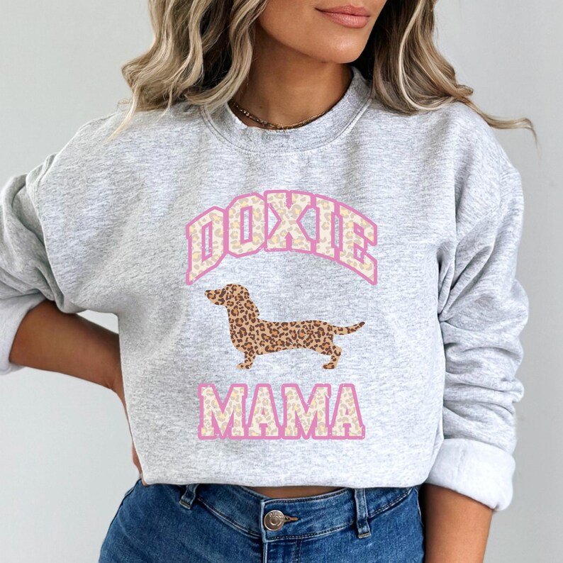 May include: A gray sweatshirt with a pink and white graphic of a dachshund with a leopard print pattern. The text "DOXIE MAMA" is printed below the dog.