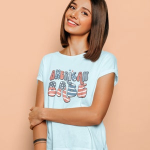 May include: A light blue t-shirt with the text "AMERICAN BABE" in a retro font with red, white, and blue stars and stripes.