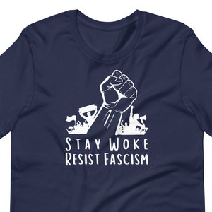 May include: Navy blue t-shirt with a white graphic of a raised fist and the text "Stay Woke Resist Fascism".