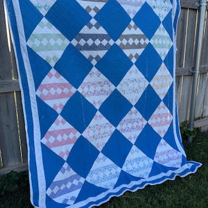 May include: A rectangular quilt featuring a repeating diamond pattern. The design consists of large solid blue diamonds interspersed with smaller diamonds containing various floral and geometric prints in shades of pink, green, brown, and white.