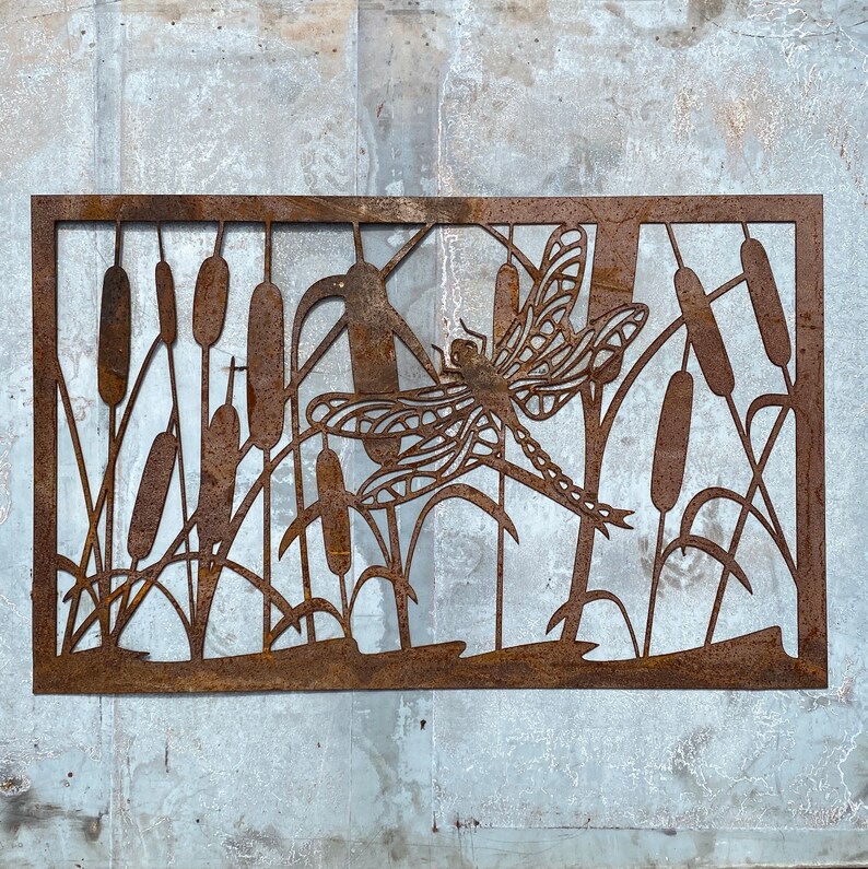 Pu&ograve; includere: Un'opera d'arte murale in metallo che raffigura una libellula con dettagli intricati, su uno sfondo di canne stilizzate. Il pezzo &egrave; di colore marrone ruggine e ha un'estetica rustica e vintage.
