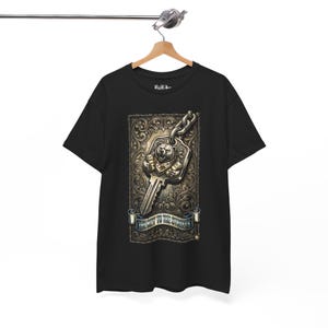 Può includere: T-shirt nero con una grafica dettagliata di una chiave con un design a orso. La chiave è attaccata a una catena e posta su uno sfondo ornato. Un banner in basso recita "The Key to the Wonders".