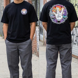 Könnte beinhalten: Schwarzes T-Shirt mit farbenfrohen Grafiken auf der Vorder- und Rückseite. Die vordere Grafik ist ein Friedenszeichen mit einem Sonnenuntergangsdesign. Die hintere Grafik zeigt eine Hand, die ein Friedenszeichen mit den Worten "CALI" und "WEST SIDE" formt.