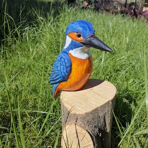 Könnte beinhalten: Eine Keramik-Vogelskulptur eines Eisvogels in den Farben Blau, Orange und Weiß. Der Vogel sitzt auf einem Baumstumpf.