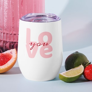 Peut inclure: Gobelet à vin isotherme blanc avec couvercle transparent. Le gobelet porte les mots "Love you" en lettres roses. L'image comprend une tranche de pamplemousse, du citron vert et une fraise.