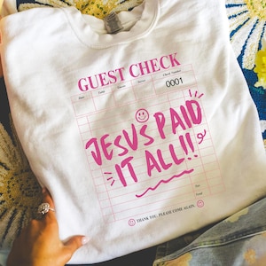 May include: White crew neck sweatshirt with a pink graphic of a guest check that reads "GUEST CHECK" and "JESUS PAID IT ALL!!". The sweatshirt has a smiley face and the text "THANK YOU, PLEASE COME AGAIN."