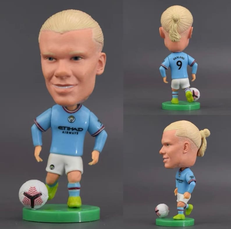 Może przedstawiać: Niebieska i biała figurka bobblehead piłkarza z blond warkoczem. Figurka ma na sobie niebieską koszulkę z napisem "ETIHAD AIRWAYS" i numerem "9" z tyłu. Figurka trzyma piłkę nożną i stoi na zielonej podstawie.