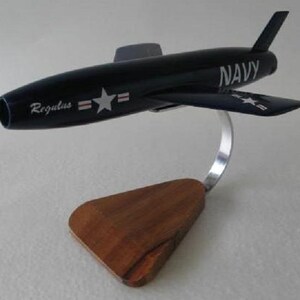 May include: A dark navy blue model airplane with the word "NAVY" and "Regulus" printed on the fuselage. The model has a silver stand and a wooden base. The wings have white star accents.