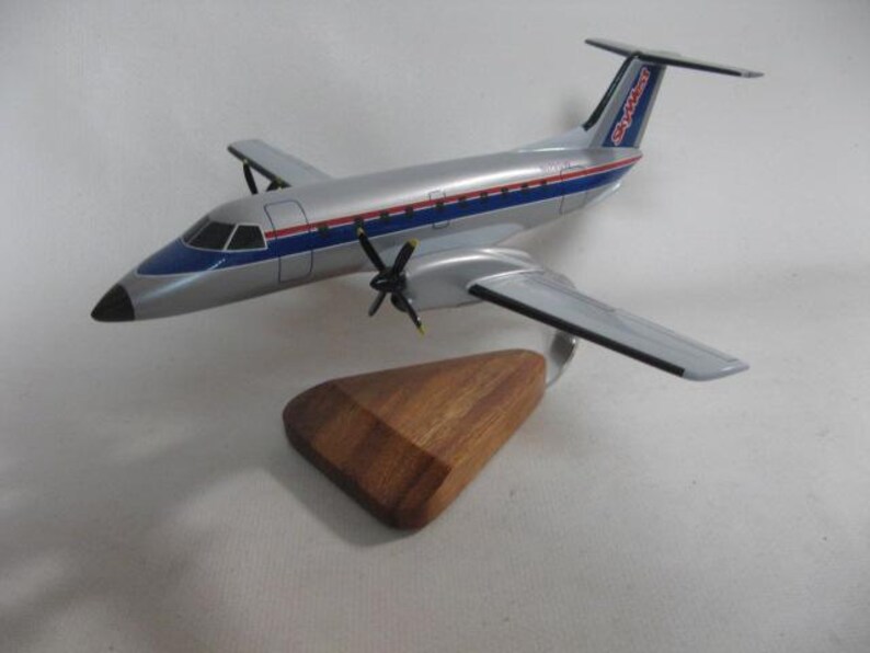 May include: A silver and blue model airplane with red and blue stripes, and the text "SkyWest" on the tail. The airplane has two propellers and is mounted on a wooden stand. A detailed miniature of a commercial aircraft.