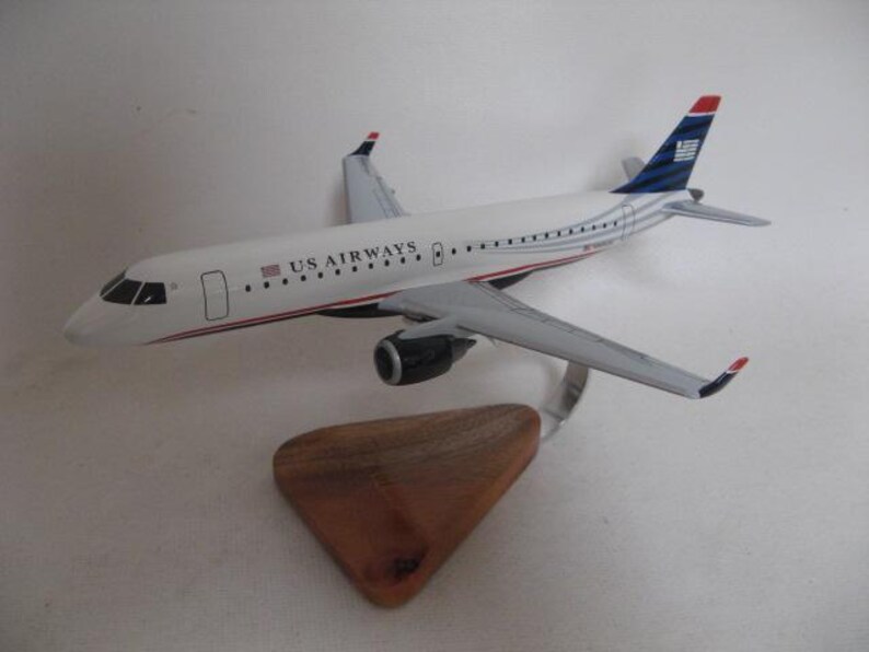 Puede incluir: Maqueta de avi&oacute;n de US Airways, blanca con detalles rojos y azules. El avi&oacute;n est&aacute; sobre un soporte de madera. La cola presenta un dise&ntilde;o azul y blanco. Las alas son grises.