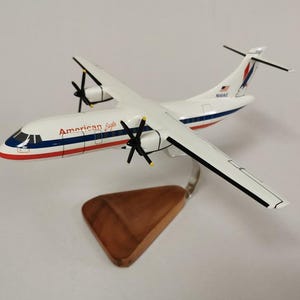 May include: A white and blue model airplane with the words "American Eagle" on the side. The model has two propellers and is mounted on a wooden stand. The plane has red and blue stripes.