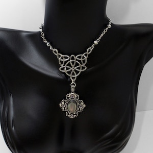 May include: A silver Celtic knot necklace with a gray oval pendant and small silver beads. The pendant has a cross-shaped design with a gray stone in the center.
