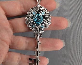 May include: A silver key pendant necklace with a large blue crystal surrounded by smaller blue crystals and intricate silver filigree.