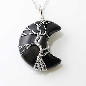 May include: A silver wire wrapped tree of life pendant with a black crescent moon shaped gemstone.
