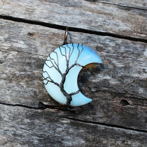 May include: A crescent moon shaped pendant with a wire wrapped tree design. The moon is made of blue and white opal.