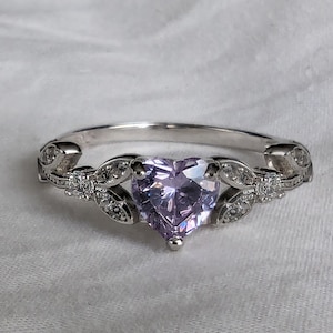 May include: A silver ring with a delicate, leafy design and a large, heart-shaped purple gemstone.