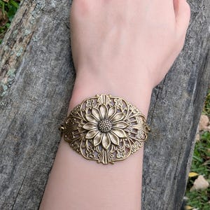 Vintage brass sunflower bracelet with leaf detail displayed on wrist over a log.