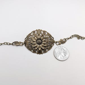 Vintage brass sunflower bracelet with leaf detail laying against nuetral background with quarter for size comparison.