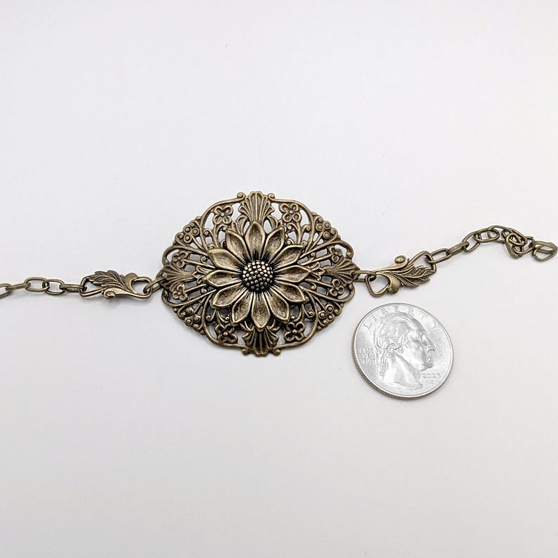 Vintage brass sunflower bracelet with leaf detail laying against nuetral background with quarter for size comparison.
