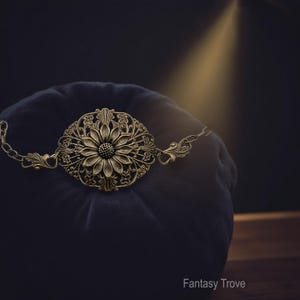 Vintage brass sunflower bracelet with leaf detail displayed on dark velvet pillow.