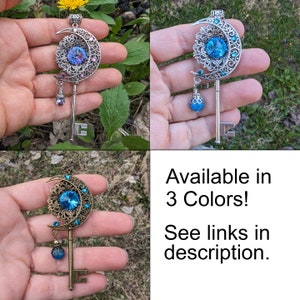 Puede incluir: Tres colgantes decorativos de llave en plata, azul y bronce. Cada llave presenta un dise&ntilde;o de luna creciente y sol con una gran gema central y una cuenta colgante. Texto: &iexcl;Disponible en 3 colores! Ver enlaces en la descripci&oacute;n.
