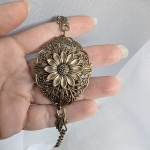 Vintage brass sunflower bracelet with leaf detail held in hand.