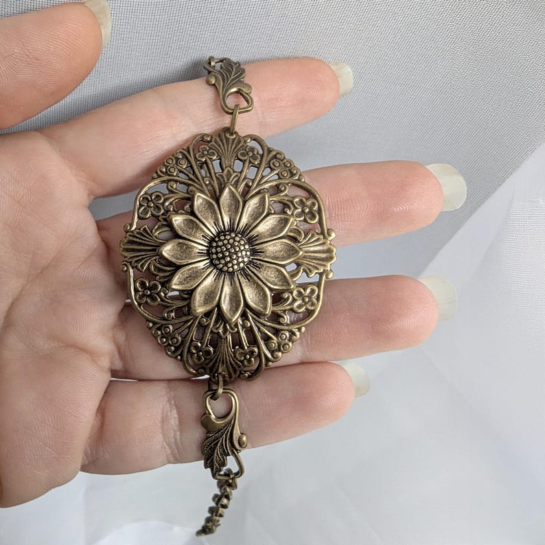 Vintage brass sunflower bracelet with leaf detail held in hand.