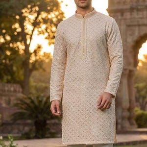 May include: A cream-colored kurta with intricate embroidery and a mandarin collar. The long-sleeved tunic is paired with white pants. The word "Chiku" is displayed in a white box at the bottom of the image. The outfit is suitable for formal occasions.