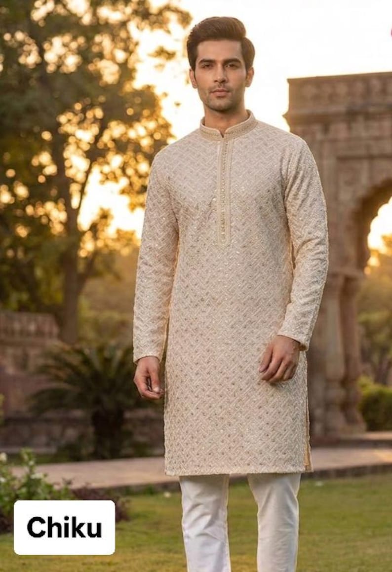 May include: A cream-colored kurta with intricate embroidery and a mandarin collar. The long-sleeved tunic is paired with white pants. The word "Chiku" is displayed in a white box at the bottom of the image. The outfit is suitable for formal occasions.