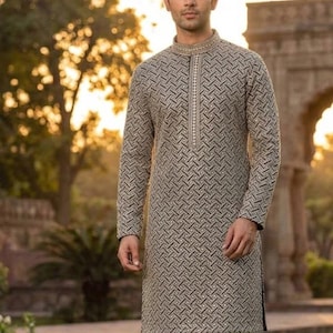 May include: A long-sleeved, patterned tunic in shades of gray and black, paired with white pants. The tunic features a mandarin collar and a vertical zipper. The word "Black" is displayed in a black box at the bottom.