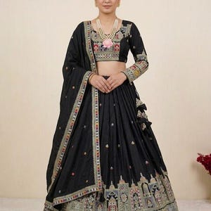 May include: A black lehenga choli set featuring a cropped blouse with long sleeves and a full-length skirt. Both pieces are adorned with intricate, multi-coloured embroidery along the hemlines and cuffs, complemented by a matching black dupatta.
