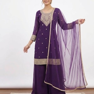 May include: A purple salwar kameez set with gold embroidery. The set includes a long-sleeved tunic, wide-legged pants, and a sheer dupatta. The tunic and pants feature gold trim and the tunic has detailed embroidery around the neckline.