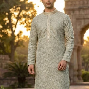 Può includere: Un kurta verde chiaro con ricami intricati e colletto alla coreana. La tunica a maniche lunghe è abbinata a pantaloni bianchi. La parola "Pista" è visualizzata in un riquadro verde in basso a destra.