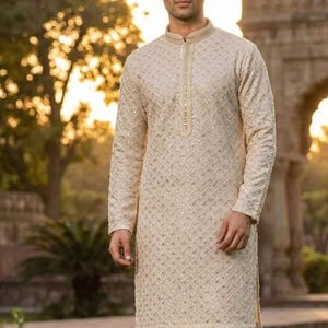 May include: Cream-colored kurta with intricate embroidery and a mandarin collar. The long-sleeved tunic is paired with white pants. The image has the word "White" in a white box at the bottom.