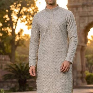 May include: A light grey kurta with a geometric pattern and long sleeves. The kurta has a mandarin collar and is paired with white pants. The outfit is suitable for formal occasions.