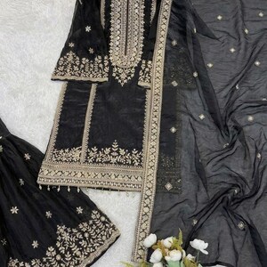 Puede incluir: Conjunto de salwar kameez negro bordado en dorado. El conjunto incluye una t&uacute;nica, pantalones y una bufanda transparente. La t&uacute;nica y los pantalones presentan intrincados bordados dorados. La bufanda tiene delicados adornos dorados.