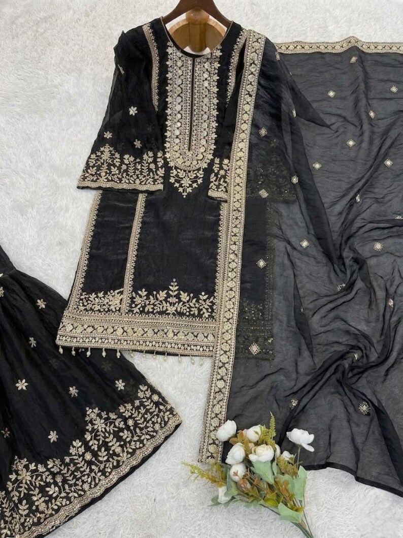 Puede incluir: Conjunto de salwar kameez negro bordado en dorado. El conjunto incluye una t&uacute;nica, pantalones y una bufanda transparente. La t&uacute;nica y los pantalones presentan intrincados bordados dorados. La bufanda tiene delicados adornos dorados.