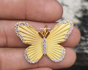 May include: A gold-colored butterfly pendant with intricate detailing. The wings feature a textured, fan-like design, and are outlined with small, clear stones. The center of the butterfly and the antennae are also adorned with stones. The brand name "Angiekrafts" is visible.