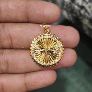 Puede incluir: Pendiente de oro con un diseño circular que presenta una cruz con pequeñas piedras blancas alrededor del borde.