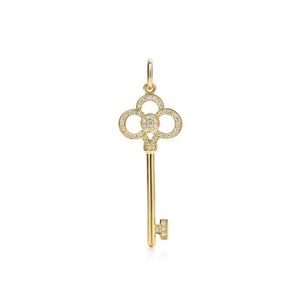 Puede incluir: Un colgante de llave de oro con un diseño engastado en diamantes. La llave tiene una cabeza en forma de trébol y un eje largo y delgado.