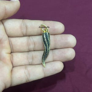 May include: A gold-toned pendant shaped like a black horn with black gemstones. The pendant is held in a hand.