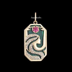 Puede incluir: Colgante de oro con un perfil de mujer sobre un fondo de malaquita verde. El cabello de la mujer está adornado con diamantes blancos. Un círculo de piedras preciosas rosas se encuentra sobre la cabeza de la mujer. El colgante es rectangular con bordes redondeados.