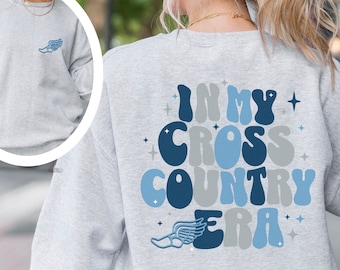 May include: A gray sweatshirt with the text "In My Cross Country Era" in blue and gray letters with a blue running shoe with a wing on the back.