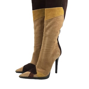 May include: A pair of brown, tan, and yellow suede knee-high boots with a pointed toe and stiletto heel.